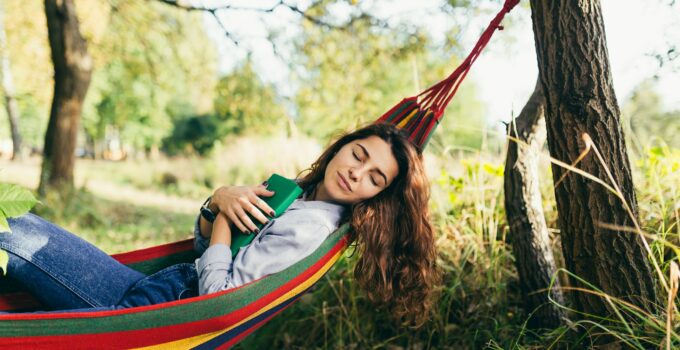 Young beautiful woman resting in nature, lying in a hammock, reading a book, vacation